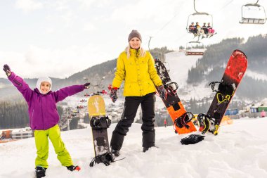 Anne ve kızı kış tatilinde snowboard yapıyor.
