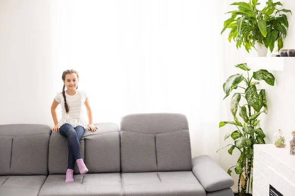 Brunett liten flicka i gul blus på en soffa hemma. — Stockfoto