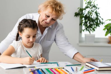 Kadın öğretmen ya da koruyucu anne, beyaz bir kız öğrencinin masada oturup ödevlerini yapmasına yardım ediyor. Çeşitli dadılar ve çocuklar evde ders çalışarak not defterinde yazmayı öğreniyorlar..