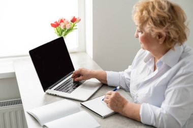 Evde dizüstü bilgisayar kullanan bir kadın emeklinin yan görüntüsü