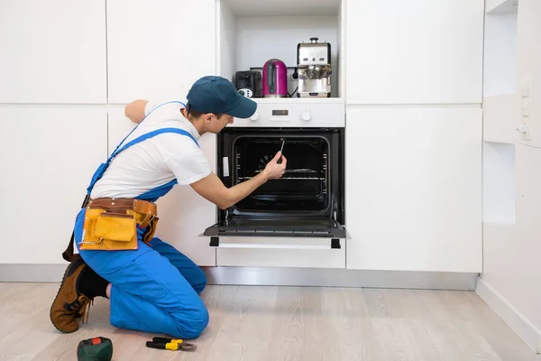 Junger Reparateur in Schutzkleidung repariert Ofen in Küche — Stockfoto