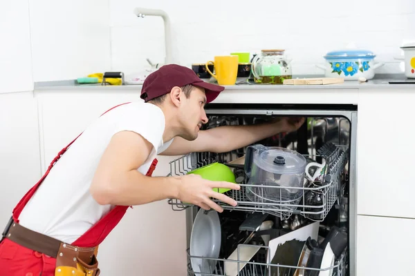 Glücklicher Meister. Männlicher Techniker sitzt neben Spülmaschine mit Schraubenzieher in Küche mit Instrumenten und lächelt — Stockfoto