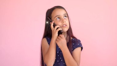 Elinde cep telefonu olan, pembe elbiseli küçük anaokulu kızı.