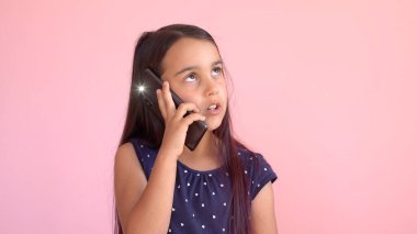 Elinde cep telefonu olan, pembe elbiseli küçük anaokulu kızı.