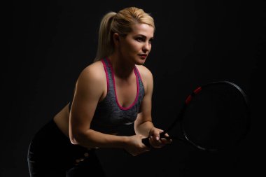 Genç bayan tenisçi siyah arka planda raketle poz veriyor.