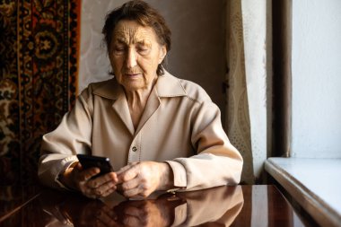 Çok yaşlı bir kadın evde akıllı telefon kullanıyor..