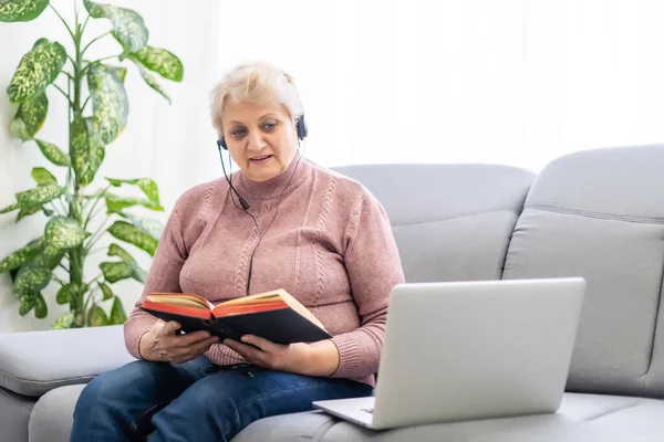 Äldre kvinna med bibel och bärbar dator framför henne ansluten till online kyrkotjänster urring covid 19 utbrott — Stockfoto