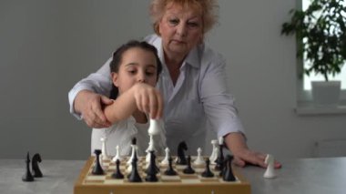 Büyükanne ve genç kız evde birlikte satranç oynuyorlar.