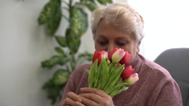 O bătrână frumoasă mirosind un buchet de lalele — Videoclip de stoc