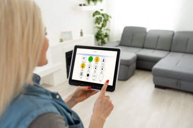 Akıllı ev kavramı. Genç bir kadın tablet üzerinde akıllı ev uygulaması kullanıyor.