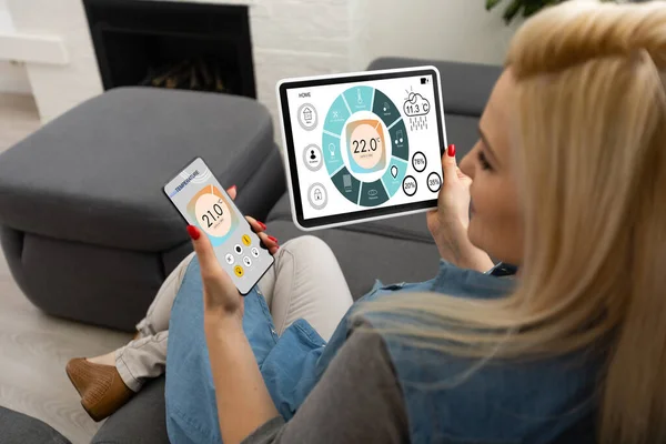 Home temperature, safety and environment control on mobile app. Smart phone in woman hand. Living room in background