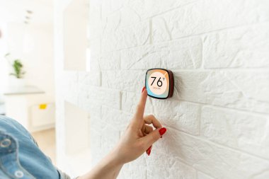Akıllı ev dijital termostatı dokunmatik ekranlı kadın oturma odasının duvarındaki ısıyı ayarlamak için dokunmatik ekrana dokunuyor