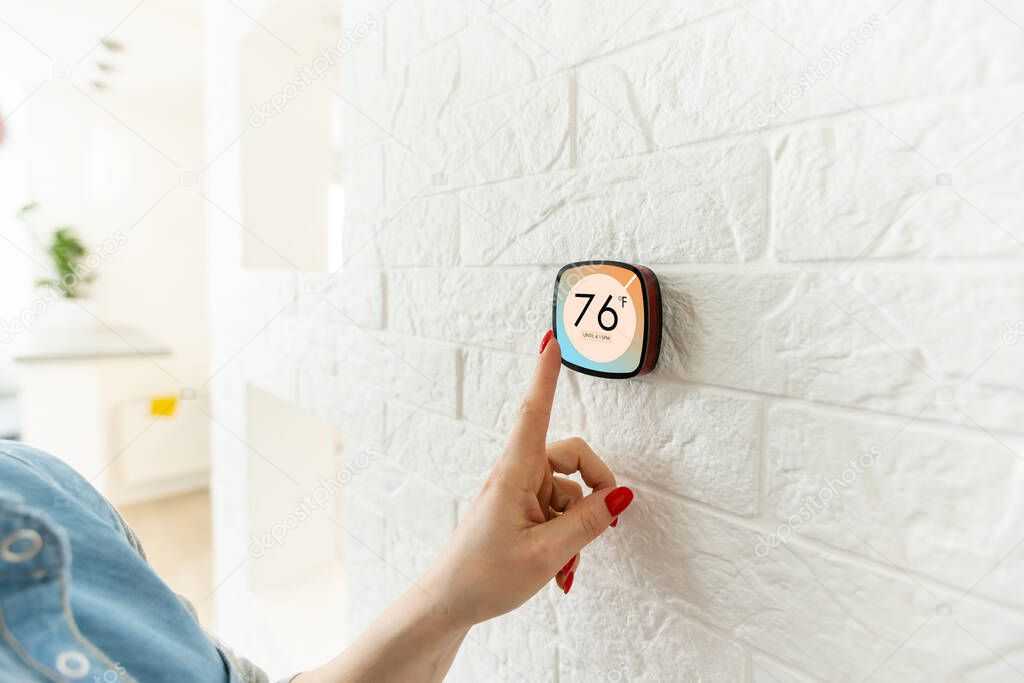 Smart home digital thermostat touch screen woman touching touchscreen to adjust temperature of heating in living room wall