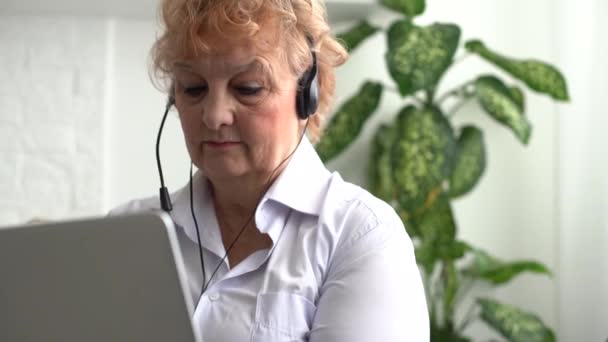 Een oudere vrouw houdt een laptop vast en belt. Oma geniet van site support — Stockvideo