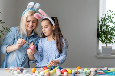 Mutlu Paskalyalar. Bir anne ve kızı Paskalya yumurtası boyuyor. Mutlu aile Paskalya için hazırlanıyor. Paskalya günü tavşan kulağı takan şirin bir kız çocuğu..