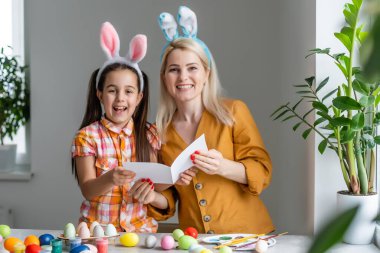 Anne ve kızı yumurta boyuyor. Mutlu aile Paskalya için hazırlanıyor. Tavşan kulağı takan şirin bir kız çocuğu..