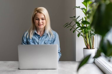 İşine odaklan. Akıllı, rahat giyinen, kendine güveni tam genç bir kadın kreatif ofis veya kafenin penceresinin yanında otururken dizüstü bilgisayarla çalışıyor.