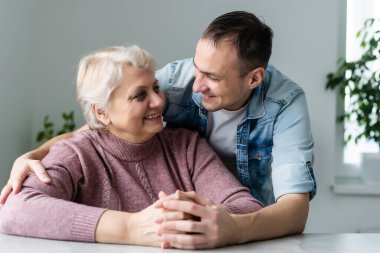 Anne ve yetişkin oğul birlikte, oğul anneye öpücük veriyor.