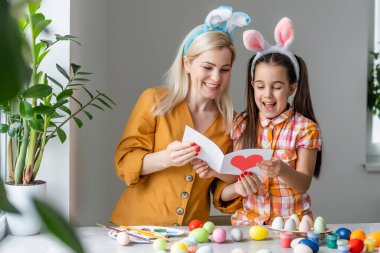 Anne ve kızı birlikte kutlama konseptinde oturup tebrik kartı okuyorlar.