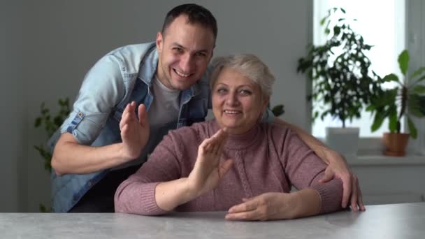 Cabeça tiro jovem barbudo feliz abraçando bela mãe smiling meia-idade sênior em óculos, relaxando juntos no sofá confortável na sala de estar, desfrutando de conversa engraçada ou fofocas — Vídeo de Stock