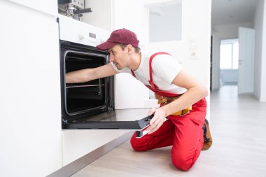 Mutfakta fırın tamirinde çalışan genç bir tamirci.