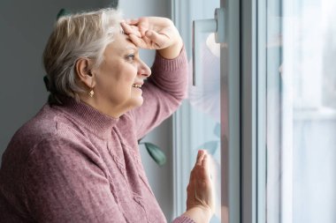 Yaşlı kadın evde dinleniyor. Pencerenin yanında duruyor. Yaşlılar için yakın plan bir yaşam tarzı.