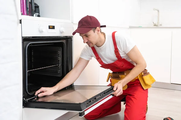 Schöner junger Reparateur, der mit einem Schraubenzieher den Ofen repariert — Stockfoto