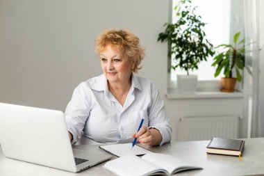 Yaşlı bir kadın online iletişim için dizüstü bilgisayar tutuyor.