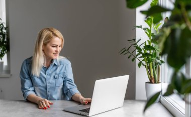 İşine odaklan. Akıllı, rahat giyinen, kendine güveni tam genç bir kadın kreatif ofis veya kafenin penceresinin yanında otururken dizüstü bilgisayarla çalışıyor.