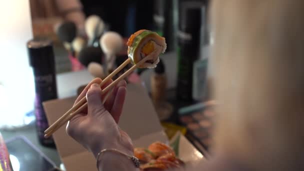 Όμορφη νεαρή γυναίκα τρώει ρολό σούσι. Γυναίκα τρώει σούσι με ξυλάκια. — Αρχείο Βίντεο