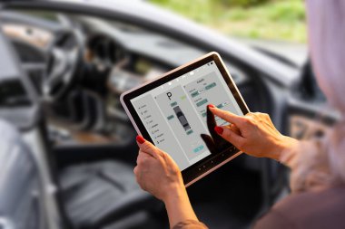 Dışarıdaki aracın yanında dururken mobil uygulamalı arabayı kontrol eden kadın, uygulama arayüzü ile tabletin yakın görüntüsü