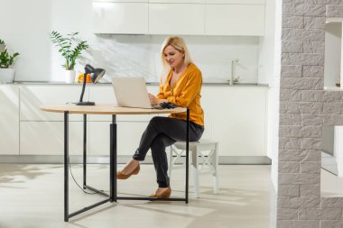 Parlak mutfakta dizüstü bilgisayarla çalışan kadın portresi. Covid-19 koronavirüs. Sosyal uzaklık