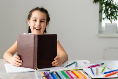 Sevimli küçük kız evde çalışıyor ve gülümsüyor.