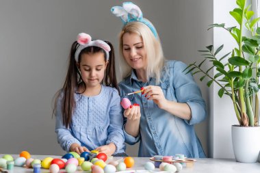 Anne ve kızı yumurta boyuyor. Mutlu aile Paskalya için hazırlanıyor. Tavşan kulağı takan şirin bir kız çocuğu..