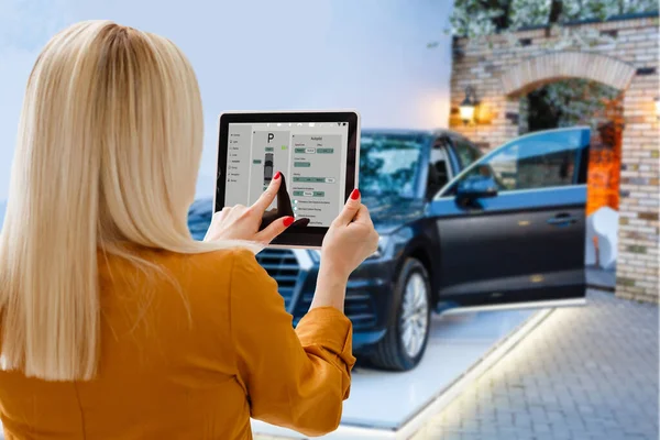 Woman controlling car with tablet application while standing near the vehicle outdoors, close-up view on the tablet with app interface
