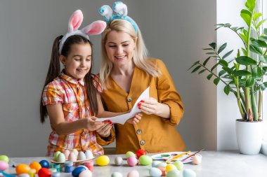 Mutlu Paskalyalar. Bir anne ve kızı Paskalya yumurtası boyuyor. Mutlu aile Paskalya için hazırlanıyor. Paskalya günü tavşan kulağı takan şirin bir kız çocuğu..