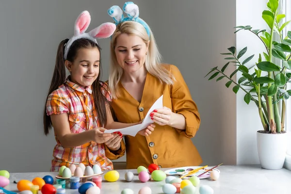 Mutlu Paskalyalar. Bir anne ve kızı Paskalya yumurtası boyuyor. Mutlu aile Paskalya için hazırlanıyor. Paskalya günü tavşan kulağı takan şirin bir kız çocuğu..