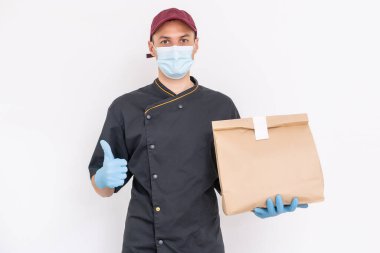 Koruyucu maskeli ve eldivenli teslimatçı, bir binanın önünde poşet dolusu erzak..