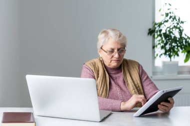 Ciddi, olgun yetişkin bir kadın laptopta antrenman videosu izliyor. Evden ya da ofisten çalışıyor. 60 'ların orta yaşlı iş kadını bilgisayar teknolojisi kullanırken not alıyor