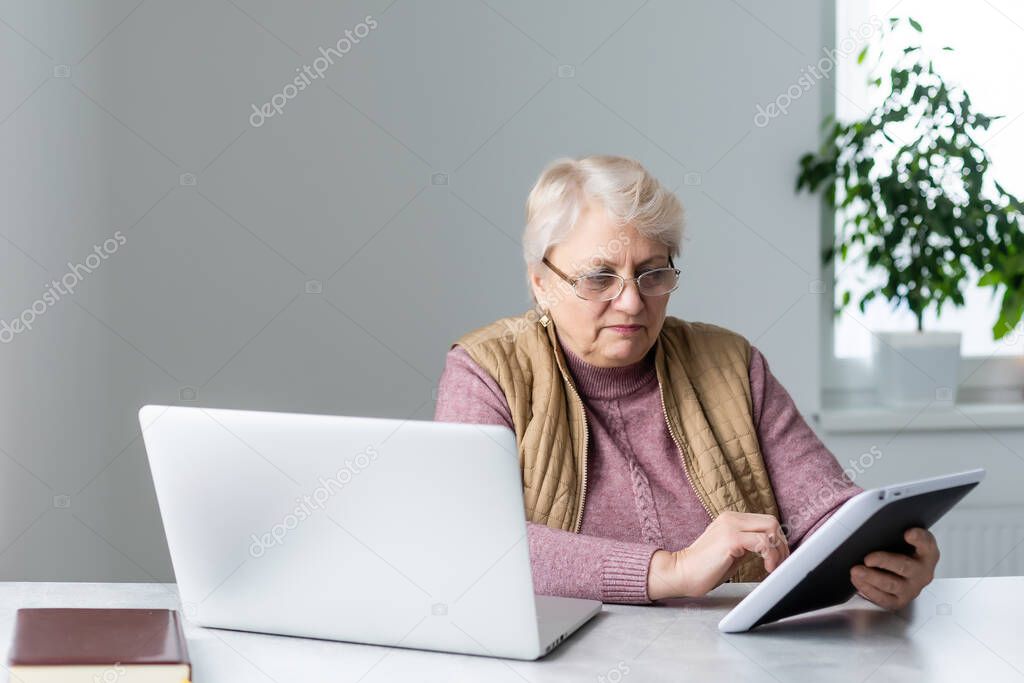 Serious mature older adult woman watching training webinar on laptop working from home or in office. 60s middle aged businesswoman taking notes while using computer technology