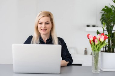 Genç ve güzel bir kadın evde dizüstü bilgisayar kullanıyor.