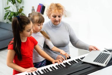 Güzel yaşlı kadın küçük torunlarına sentezleyici çalmayı öğretiyor. Genç büyükanne torunları için piyano çalar..