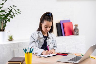 Küçük kız ödevini evde yapıyor ve dizüstü bilgisayar kullanıyor.