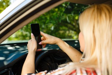 Genç bayan sürücü dokunmatik ekranlı akıllı telefon ve GPS kullanarak bir arabada geziniyor..