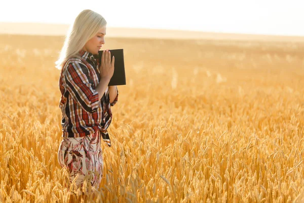 Christian woman praying on holy bible and wooden cross in barley field on summer. Woman pray for god blessing to wishing have a better life and believe in goodness.