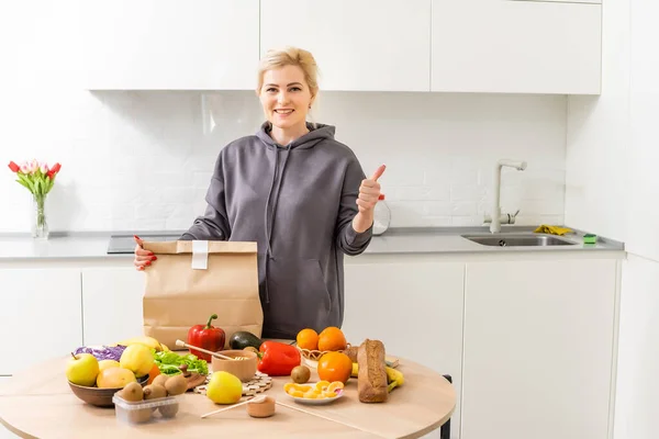 Woman sorts out purchases in the kitchen. Grocery delivery in paper bags. Subscription service from grocery store in conditions of quarantine because of coronavirus COVID19