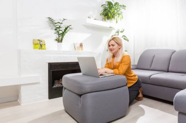 Evde dizüstü bilgisayarıyla çalışan güzel genç bir kadın.