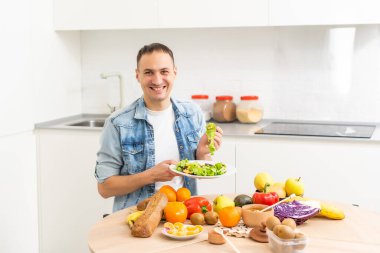 Mutlu genç adam romantik bir akşam yemeği hazırlıyor sebze tarifleri diyet menüsünü arıyor, gülümseyen koca sağlıklı vegan yemekleri pişiriyor mutfak içinde salata pişiriyor.