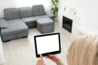 Akıllı tabletle akıllı ev uygulaması olan eller arka plan olarak ev oturma odasında..