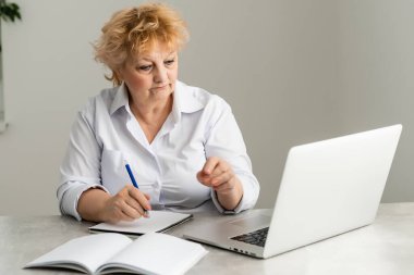 Evde dizüstü bilgisayar kullanan bir kadın emeklinin yan görüntüsü